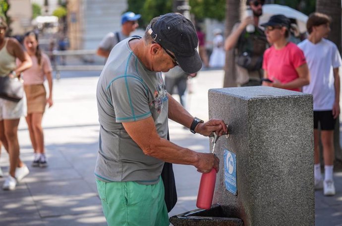 Un hombre llena una botella de agua en una fuente pública.