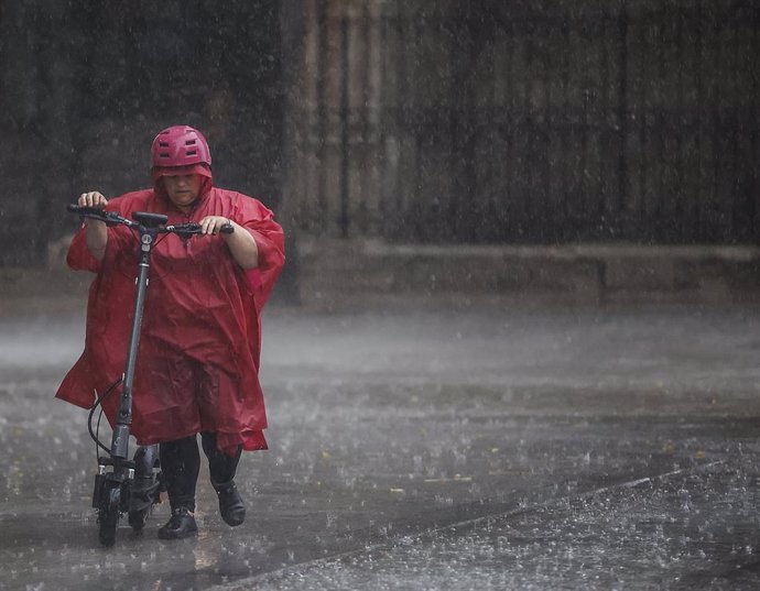 Archivo - Una persona camina bajo la lluvia