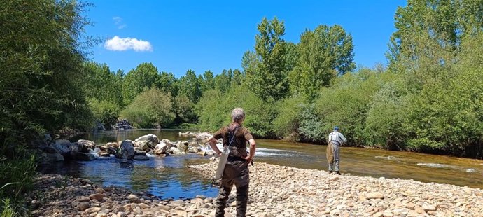 Dos hombres pescan a la orilla de un río.