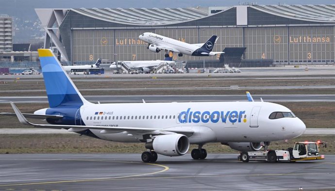 Archivo - 14 February 2024, Hesse, Frankfurt/Main: While a Lufthansa plane takes off, a Discover Airlines passenger plane is towed by a tug at Frankfurt Airport. Photo: Arne Dedert/dpa