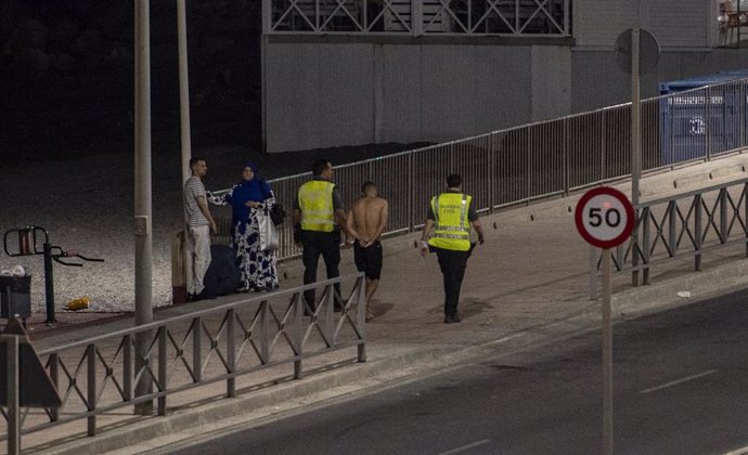 Un migrante detenido por dos agentes de la Guardia Civil tras entrar a nado por la playa del Tarajal, en Ceuta