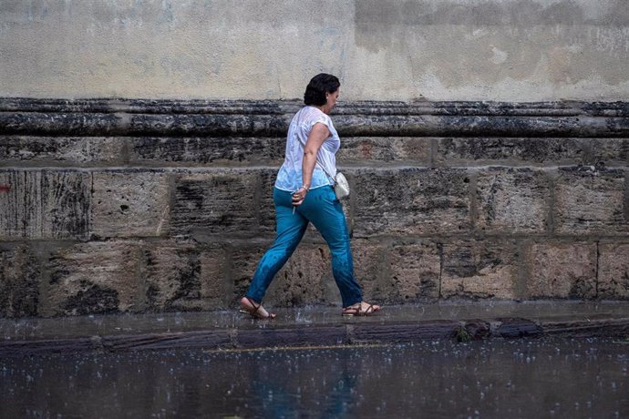 Archivo - Una mujer anda por la calle bajo la lluvia