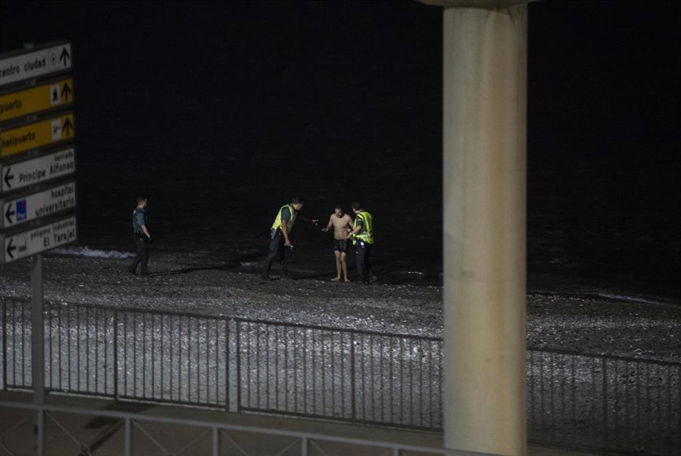 Un migrante detenido por dos agentes de la Guardia Civil tras entrar entrado a nado por la playa del Tarajal, en Ceuta