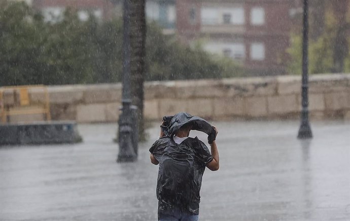 Archivo - Una persona camina bajo la lluvia