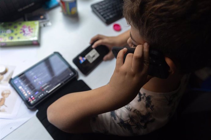 Archivo - Un niño usa el teléfono móvil y una tablet.