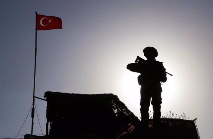 Un militar junto a una bandera de Turquía