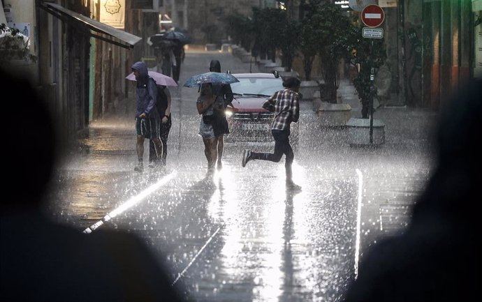 Archivo - Varias personas caminan bajo la lluvia en València