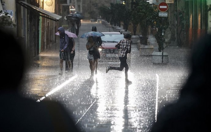 Archivo - Arxiu - Diverses persones caminen baix la pluja a València
