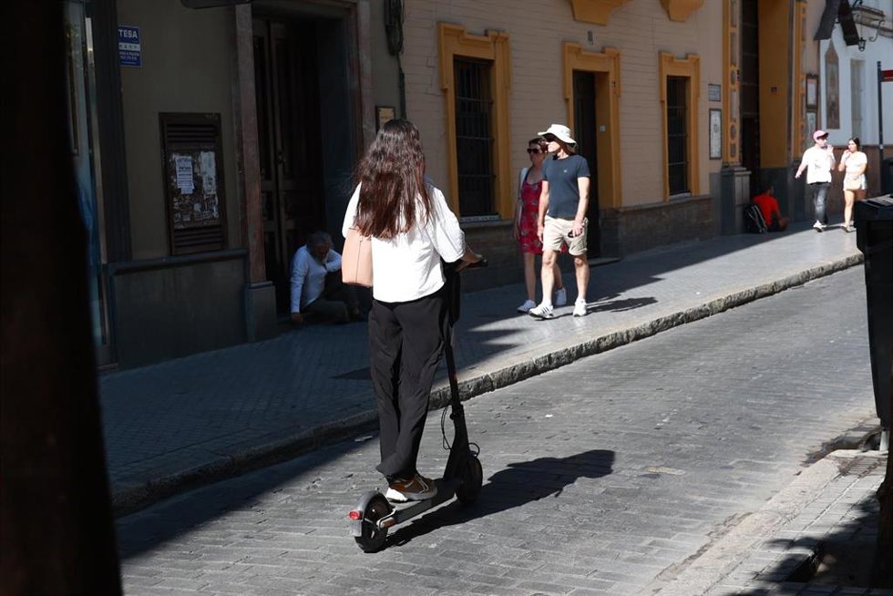 Una joven circula en un patinete eléctrico en una calle del centro de Sevilla. A 7 de agosto de 2024, en Sevilla (Andalucía, España).