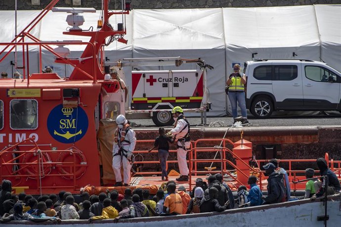 Miembros de los equipos de emergencias ayudan a desembarcar a varios migrantes de un cayuco, en el Puerto de La Restinga