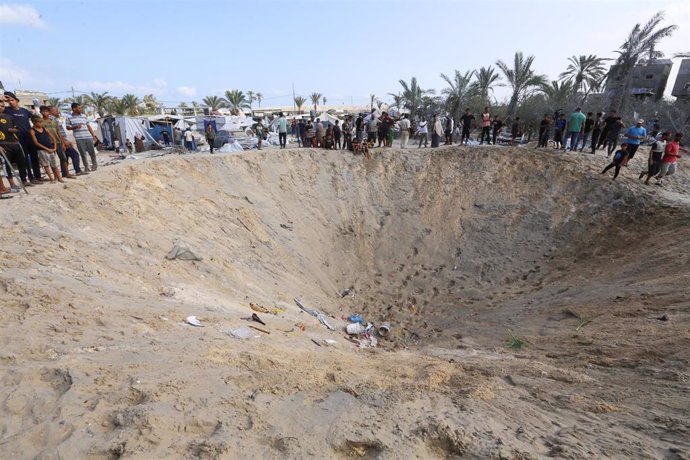 Un grupo de palestinos junto al cráter dejado por un bombardeo israelí en Al Mauasi, en el sur de la Franja de Gaza