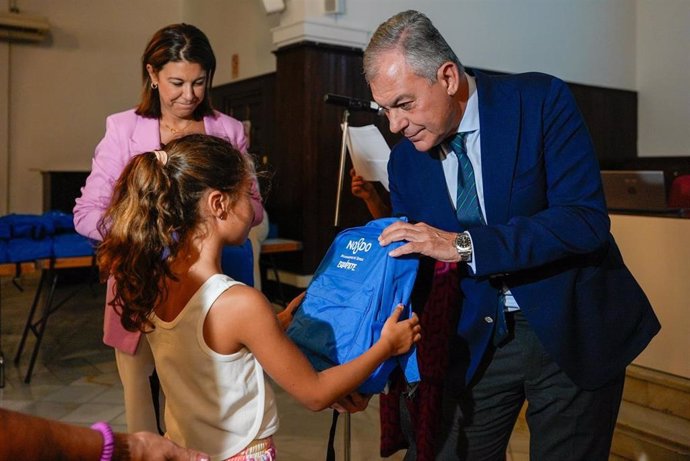 El alcalde de Sevilla, José Luis Sanz, hace entrega de una de las mochilas con material escolar gratuito a una niña.