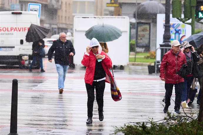 Archivo - Varias personas tratan de cubrirse de la lluvia en Santander  