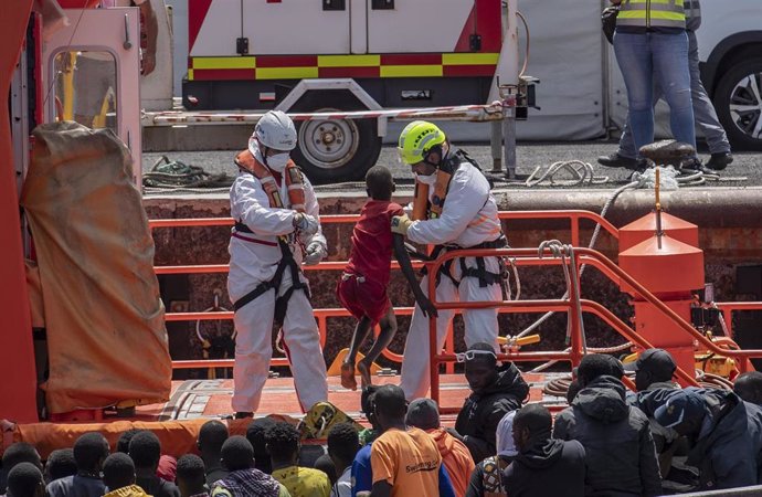 Miembros de los equipos de emergencias ayudan a desembarcar a varios migrantes de un cayuco, en el Puerto de La Restinga