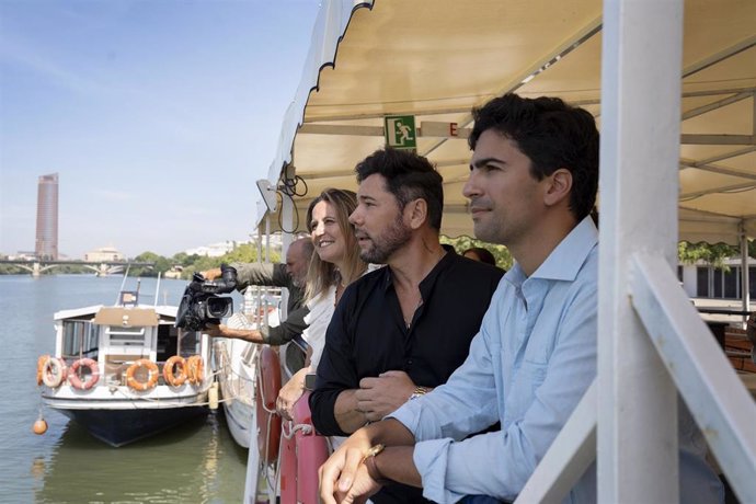 El director de la Bienal, Luis Ybarra, en primer término, y la delegada de Turismo y Cultura, Angie Moreno, acompañan a Miguel Poveda en un paseo en catamarán durante un encuentro con los medios.