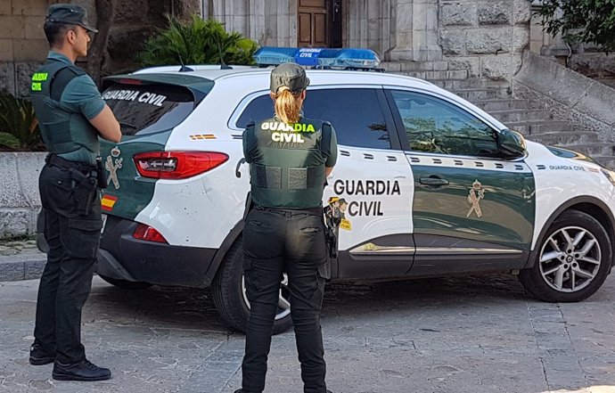 Archivo - Dos agentes de la Guardia Civil junto a un coche oficial, en imagen de archivo