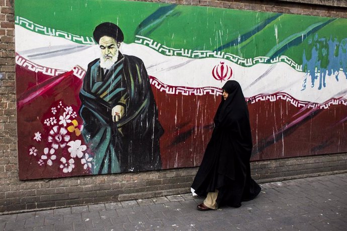 Archivo - Una mujer junto a un mural con la bandera iraní y el ayatolá Ruholá Jomeini en Teherán (archivo)