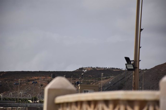 Imagen de este domingo, en la que se aprecia a migrantes agolpados en suelo marroquí frente a la frontera con Ceuta.