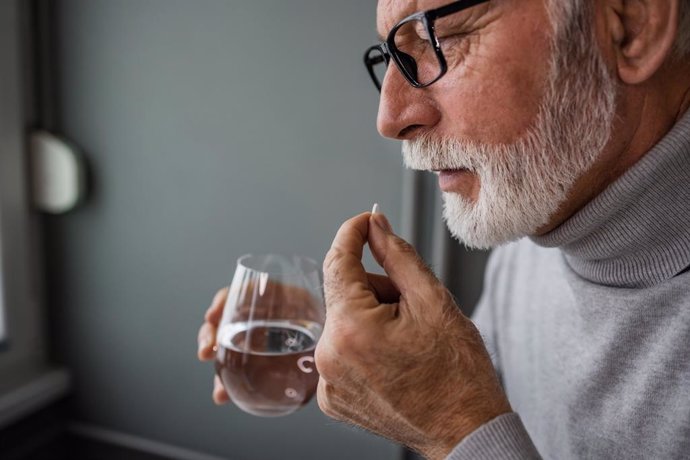 Archivo - Hombre tomando un medicamento con un vaso de agua.