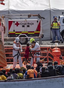 Miembros de los equipos de emergencias ayudan a desembarcar a varios migrantes de un cayuco, en el Puerto de La Restinga