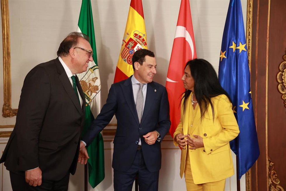 El presidente de la Junta de Andalucía, Juanma Moreno (c), saluda a la embajadora de Turquía en España, Nüket Küükel (d), en prese4ncia del consejero de Turismo y Andalucía Exterior, Arturo Bernal (i).