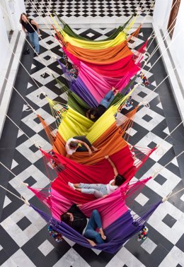 Varias personas prueban las hamacas protagonistas de la obra 'Rede Social' que se estrena en la Capilla de Afuera del Centro Andaluz de Arte Contemporáneo (CAAC).