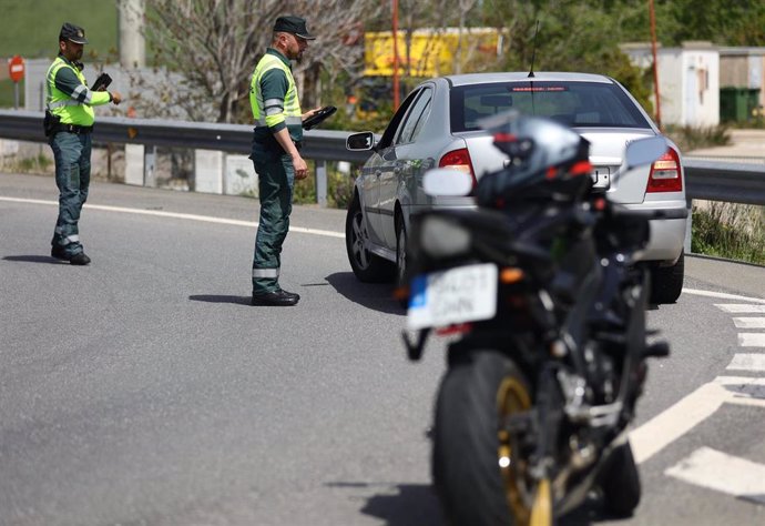 Archivo - Foto de una motocicleta. Detrás, un agente de la Guardia Civil pide documentación a un conductor  en un control de tráfico.