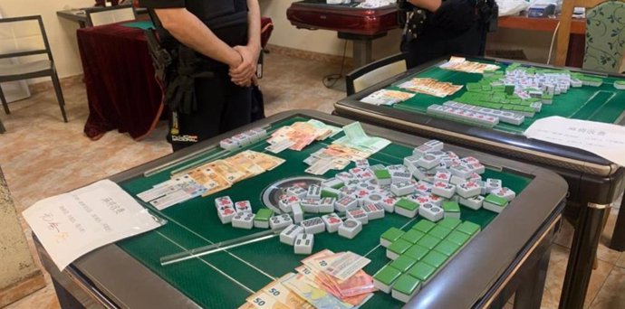 Dos agentes de la Unidad Adscrita de la Policía Nacional en el casino ilegal intervenido con dinero y fichas del Mahjong en primer término.