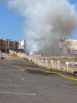 Efectivos del Consorcio de Bomberos de Tenerife trabajan en las tareas de extinción de un incendio que se ha declarado este lunes en un solar que acumulaba basura y rastrojos cerca de una nave industrial abandonada en el barrio de Taco.