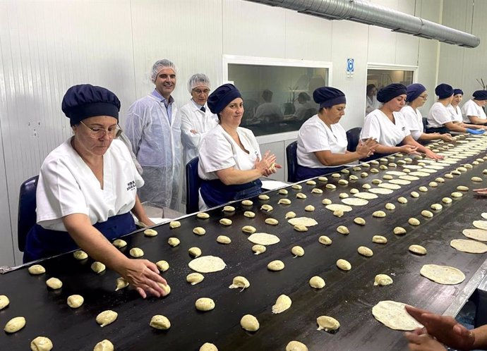 El consejero de Agricultura, Pesca, Agua y Desarrollo Rural, Ramón Fernández-Pacheco, observa cómo las 'labradoras' elaboran a mano el producto.