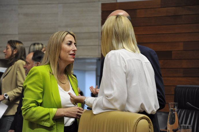 María Guardiola charla con su consejera de Hacienda al inicio del Pleno de la Asamblea.