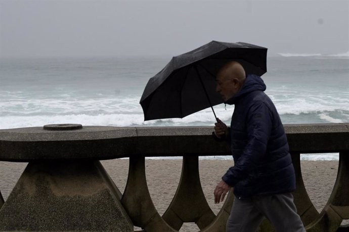 Archivo - Un hombre camina con un paraguas por la playa del Orzán, en A Coruña, Galicia (España).