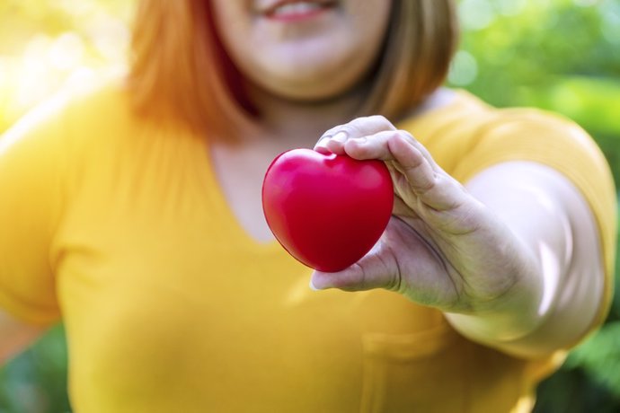 Archivo - Mujer con obesidad sujeta en su mano un corazón. Salud cardiovascular.