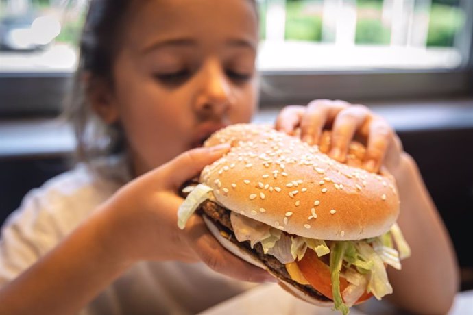 Archivo - Una niña se come una hamburguesa, de cerca