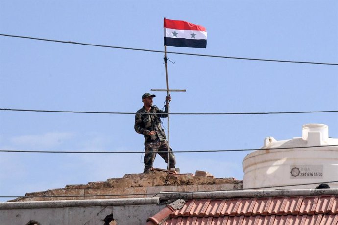 Archivo - HANDOUT - 17 October 2019, Syria, Kobane: A picture provided by the Syrian Arab News Agency (SANA) shows a Syrian army soldier holding a syrian flag as they deploying in the vicinity of Kobane. Photo: -/SANA/dpa - ATTENTION: editorial use only a