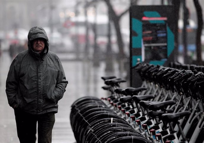 Archivo - Un hombre con un chubasquero se refugia de la lluvia.