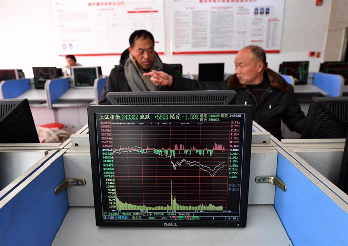 Archivo - 24 February 2022, China, Fuyang: The curve of the Shanghai Composite Index is displayed on a monitor and in the background two men talk about the stock exchange flow. 