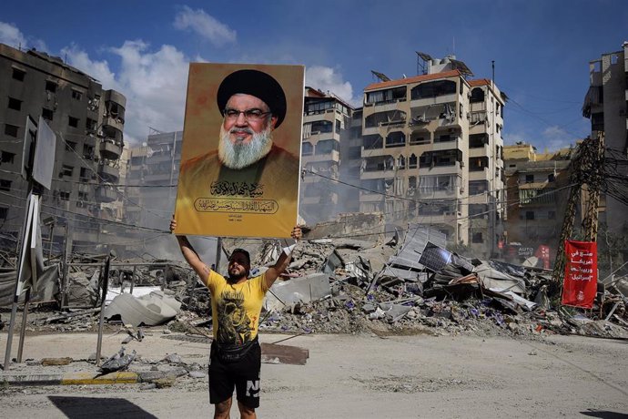 Un simpatizante de Hezbolá con un poster del líder del grupo, Hasán Nasralá, frente a un edificio bombardeado por Israel en los suburbios de Beirut (Líbano)