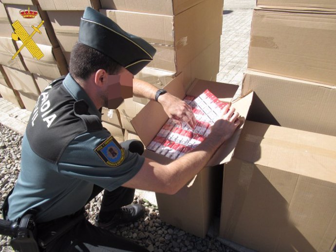 Un agente de Guardia Civil inspecciona las cajas aprehendidas a la detenida, que contienen cajetillas de tabaco.