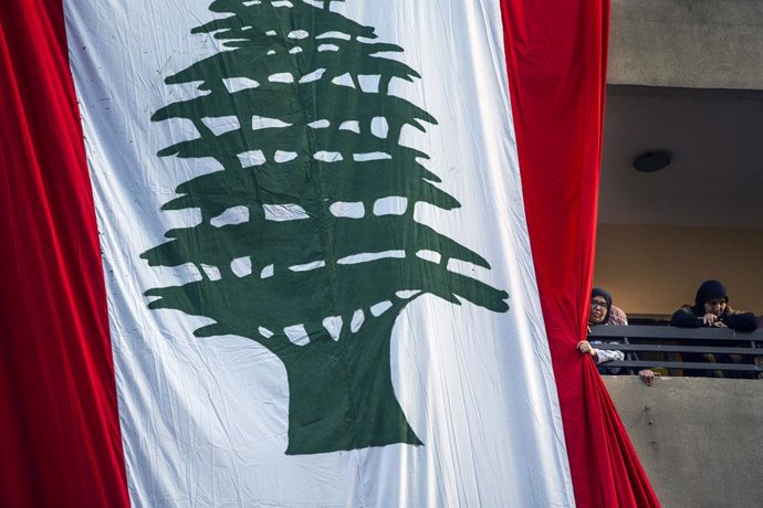 Archivo - May 17, 2021, Haret Hreik, Lebanon: A woman pushes a large Lebanese flag out of her way to watch a Hezbollah political event happening on the street below her Monday, May 17, 2021 in Haret Hreik suburbs south of Beirut, Lebanon. People who from 