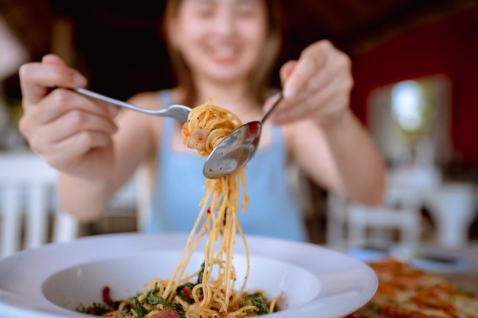 Archivo - Mujer alegre comiendo espaguetis picantes en el restaurante.