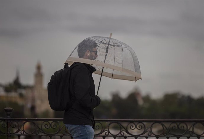 Archivo - Un hombre camina bajo la lluvia protegido bajo su paraguas durante la alerta amarilla por tormentas en Sevilla, (Andalucía, España), a 14 de mayo de 2020.