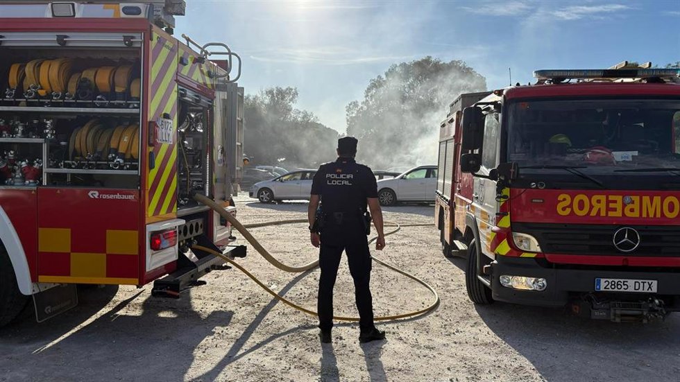 Agente de la Policía Local de Marbella entre dos camiones de bomberos en la zona de la explanada donde se produjo el incendio.