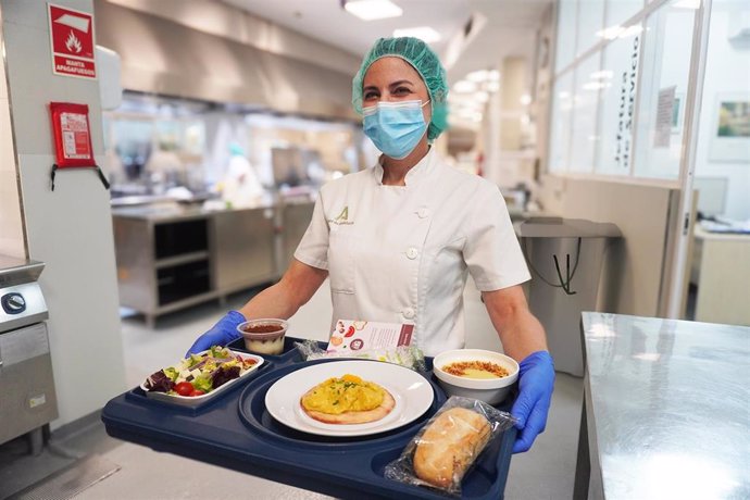 Una profesional del Servicio de Cocina porta una bandeja con un menú.