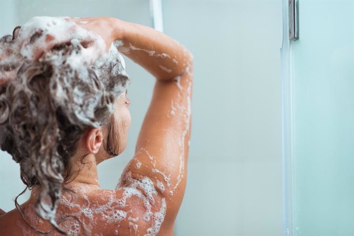 Archivo - Woman applying shampoo in shower. Rear view