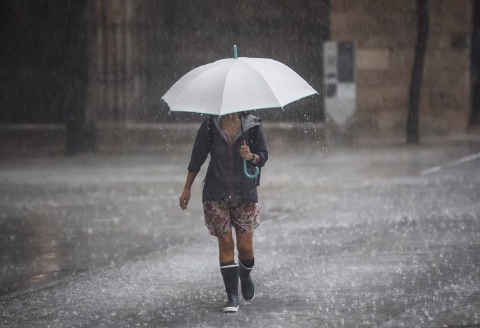 Archivo - Una persona camina amb un paraigua davall la pluja en imatge d'arxiu