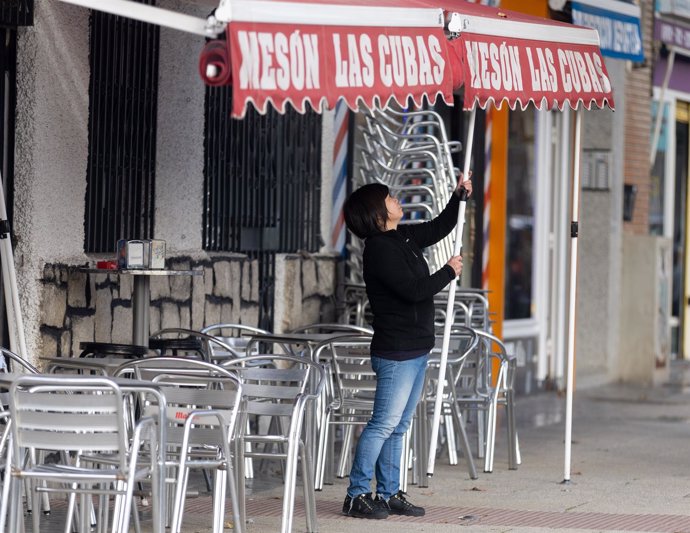 Archivo - Una camarera levanta el toldo de un bar,