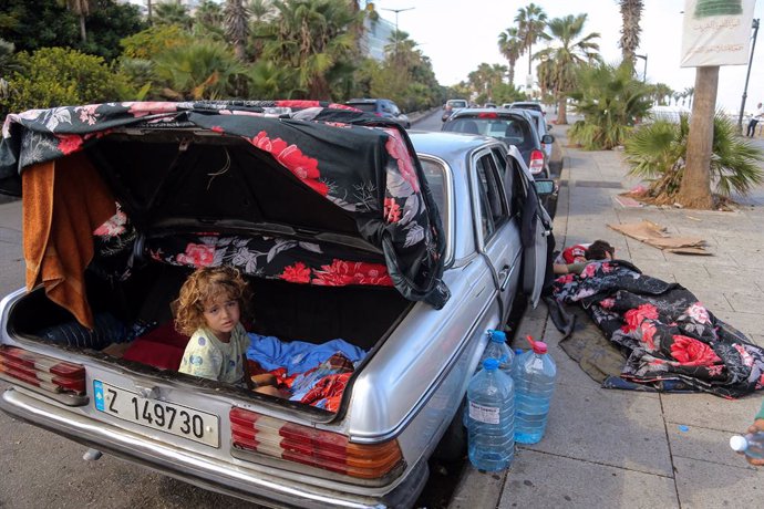 01 October 2024, Lebanon, Sidon: Abdel Salam Abdallah, a 10-year-old boy from the Lebanese southern town of Khiam sits in the trunk of his father's car after waking up from sleep. Abdel Salam's father is seen sleeping on the pavement of Beirut promenade. 