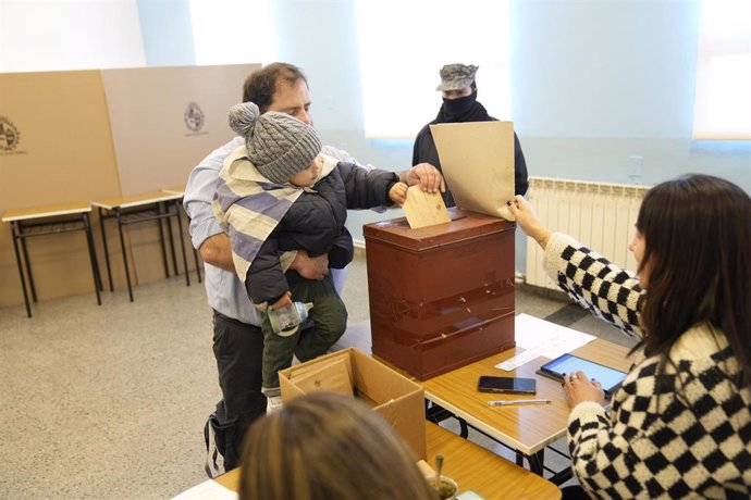 Archivo - Un ciudadano argentino con un niño en brazos deposita su voto en la urna en las primarias de Uruguay de cara a las elecciones generales de octubre