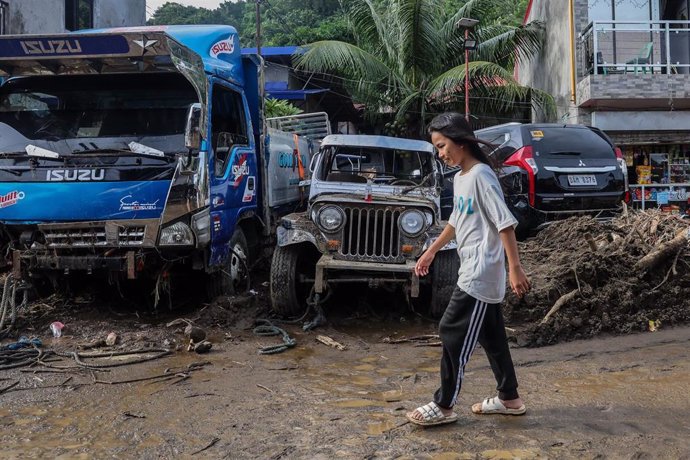 Una chica camina ante vehículos dañados por el impacto de la tormenta 'Kristine' en Batangas, Filipinas